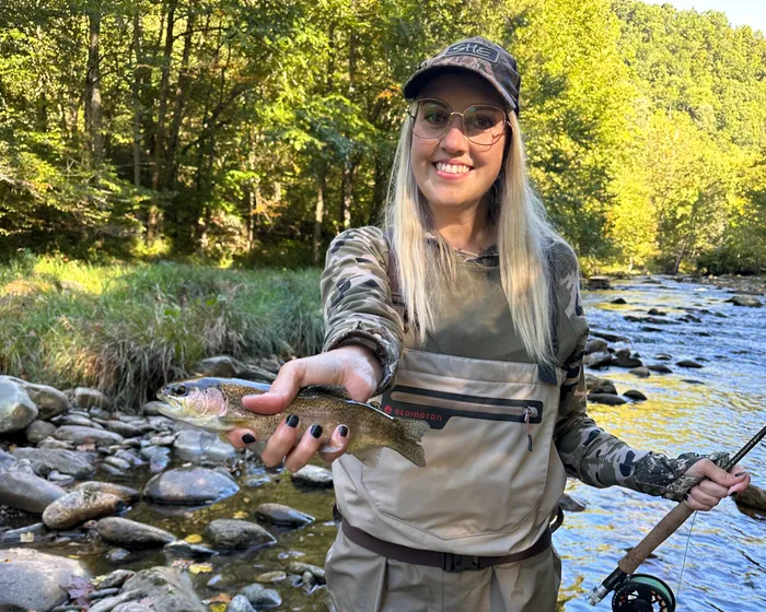 Gina fly fishing in waders on a river, holding a trout