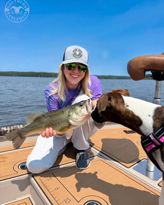 Gina on her boat holding up a largemouth bass while her dog Lacie sniffs it